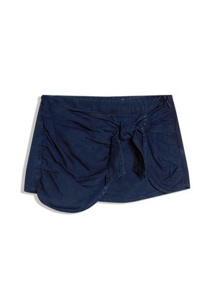 Mini-jupe en denim bleu foncé avec ourlet arrondi et détail nœud à l’avant, posée à plat sur fond blanc.