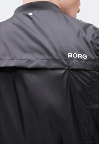 Κοντινό πλάνο του άνω μέρους της πλάτης ενός ατόμου που φοράει μαύρο μπουφάν με το κείμενο "BORG" στην περιοχή του δεξιού ώμου.