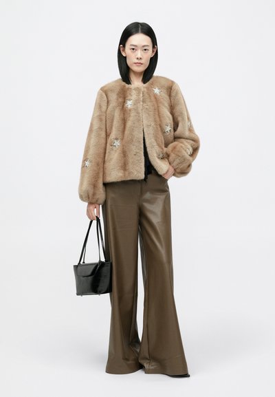 Kerged hunnik helepruuni faux karusnaha jakk, millel on hõbedased tähe kaunistused, koos kõrge vöökohtadega pruunide nahkpükstega ja musta käekotiga.