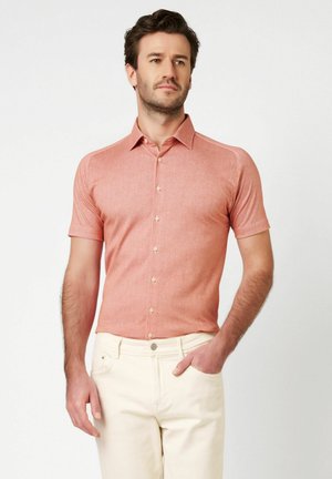 Korallenrotes Kurzarm-Hemd mit Knopfleiste und strukturierter Oberfläche, mit Kragen und dezenten Nahtdetails, kombiniert mit hellbeigen Hosen.