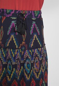 Färgglad mönstrad kjol med marinblå bas, prydd med geometriska mönster i klara färger. Elastisk midja med svart dragsko och tofsar.