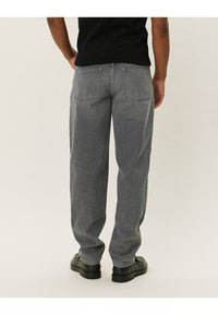 Šedé džíny z denimu se střihovým provedením regular fit, s klasickým pětipocket designem a prošitím na zadních kapsách. Nosené s černou obuví.