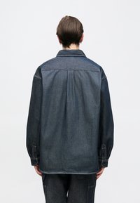 Džínová bunda s dvoubarevným designem, vybavená klasickým límcem, knoflíkovými manžetami a volným střihem. Tmavé odstíny s kontrastním prošitím.