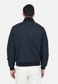 Bomber jacket blu navy con una texture liscia, polsini e orlo a costine e colletto. La vista posteriore mostra un design semplice e senza hardware visibile.