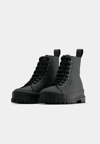 Ghete negre tip high-top cu o finisare netedă, dotate cu o talpă masivă și șireturi groase. Ochiuri întărite și bandele de prindere pentru o îmbrăcare ușoară.