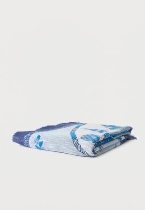 Serviette pliée à motifs bleus et blancs avec bords à franges, reposant sur un fond clair uni.