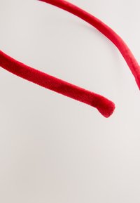 Red velvet headband with a smooth texture, slender design, and rounded ends, set against a light background.