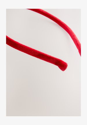 Rødt fløjls-hårbånd med glat tekstur, slankt design og afrundede ender, sat mod en lys baggrund.