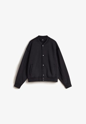 Chaqueta sudadera negra con cierre de botones a presión, puños acanalados, dos bolsillos laterales y un collar redondeado. Hecha de una tela suave con una textura lisa.