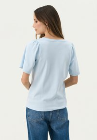 Top corto de manga corta en azul claro con hombros abullonados, cuello redondo y textura suave. Combinado con jeans de denim de cintura alta.