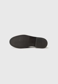 Black rubber shoe sole with smooth texture, slightly rounded shape, and a subtle embossed brand logo. Features grooves for traction.
