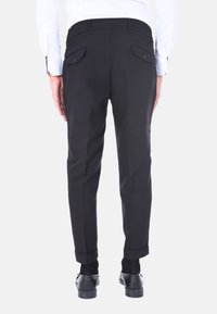 Pantaloni neri su misura con una texture liscia, dotati di due tasche posteriori con bottoni e orli arrotolati. Indossati con scarpe eleganti nere.