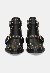 Botas de cuero negras hasta el tobillo con tachuelas doradas y acentos de hardware. Presenta múltiples correas y un diseño de punta afilada. Suela plana.