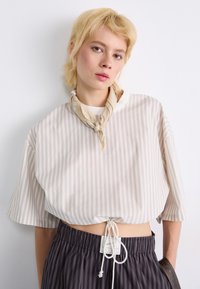 Blusa corta a righe in beige e crema, con orlo regolabile e maniche corte. Abbinata a pantaloni a righe scure con vita elastica.