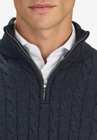 Marinblå zip-up tröja med flätad struktur, ribbat krage och dragkedjedetaljer, lagd över en vit skjorta med knappar.