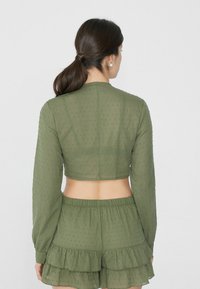 Completo a due pezzi verde oliva con top corto a maniche lunghe caratterizzato da un motivo testurizzato e pantaloni corti con orlo arricciato e vita elasticizzata.