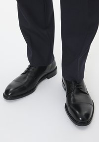 Chaussures en cuir noir avec un bout rond, un design à lacets et des détails de couture minimalistes. Associées à un pantalon texturé bleu marine.