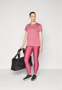 Conjunto deportivo que incluye una camiseta rosa jaspeada, leggings rosas brillantes y zapatillas negras. Se sostiene un bolsa de deporte negra en una mano.
