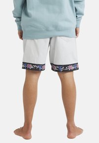 Person wearing light gray shorts with a black floral and blue bull skull pattern along the hem, paired with a light blue sweatshirt, barefoot.