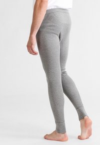 Graue, gerippte Leggings mit einer engen Passform, weicher Textur und Knöchelbündchen, von der Seite gezeigt mit sichtbaren baren Füßen.