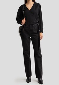 Blusa negra de envoltura con mangas largas, combinada con jeans negros de cintura alta que presentan sutiles destellos, y botines negros de tacón.