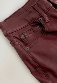 Burgundy pants with a smooth texture, featuring tonal stitching and black metal hardware on the back pocket for secure closure.