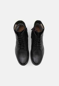 Botas de tobillo de cuero negro con un acabado suave, que presentan cordones en la parte delantera y cremalleras laterales, montadas sobre una suela de goma blanca contrastante.