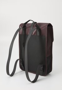 Mochila rectangular en color burdeos y negro, con correas ajustables, un asa en la parte superior y un bolsillo con cremallera lateral. Fondo liso.