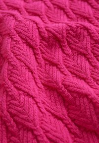 Tätstickad tyg i klarrosa, med ett strukturerat diamantmönster och upphöjda detaljer, vilket ger ett mjukt och varmt utseende.