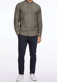 Olijfgroen overhemd met lange mouwen en een mandarinnekraag, gecombineerd met marineblauwe slim-fit broek en witte sneakers.