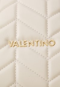 Creme læder med chevron kviltet mønster, med guld "VALENTINO" bogstaver i midten. Glat tekstur og præcise syning detaljer.