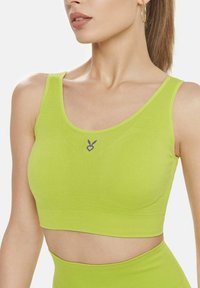 Sutien sport de culoare verde limetă, cu o textură moale, decolteu rotund și un logo în formă de inimă violetă în centru. Designul are cusături fără sudură.