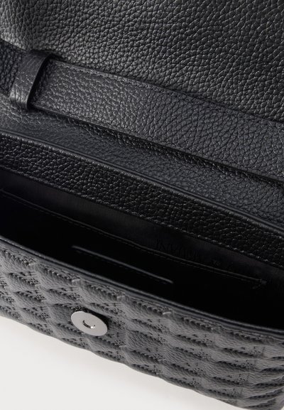 Μαύρη τσάντα χειρός από δέρμα με υφή, με ανοιχτό καπάκι που αποκαλύπτει εξωτερική επιφάνεια με ραμμένο μοτίβο και μεταλλικό κούμπωμα.