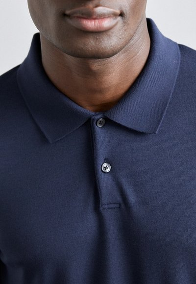 Μπλέ πόλο μπλουζάκι με υφή, κλασικό γιακά και πλέξιμο με δύο κουμπιά. Λείο φινίρισμα χωρίς σχέδια ή διακοσμήσεις.