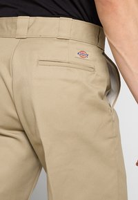 Khaki pracovní kalhoty s texturovanou tkaninou, vybavené zadní kapsou a značkovou nášivkou na pasu. Jednoduchý design, střih na míru.