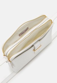 Borsa a tracolla in pelle sintetica bianca con texture effetto coccodrillo, doppio compartimento con cerniera, dettagli in oro e tracolla staccabile.