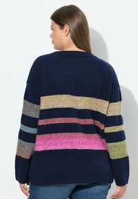 Maglione oversize blu navy con righe orizzontali in beige, rosa, verde e blu. Texture morbida e colletto a girocollo a coste.