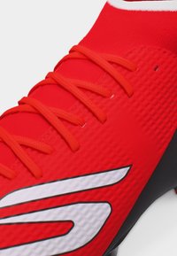 Κοντινό πλάνο κόκκινου αθλητικού παπουτσιού με κόκκινους κορδόνια και λευκό στυλιζαρισμένο λογότυπο σε υφή συνθετικού υλικού.