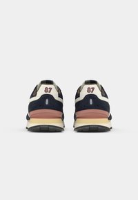 Marineblå og cremefarvede sneakers med en tekstureret ruskindsoverdel, med en lyserød accent midtsåle og nummeret "87" broderet på hælen. Sort gummisål.