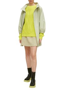 Hellgrüne wasserdichte Jacke, leuchtend gelbes strukturiertes Sweatshirt, Hahnentrittmuster-Rock und schwarze Stiefel mit limettengrünen Sohlen.