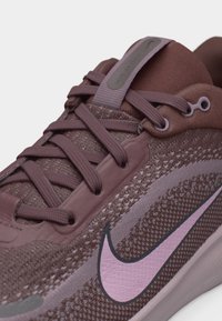 Κλείσιμο επάνω σε μοβ παπούτσι τρεξίματος Nike με υφή πλεκτού άνω μέρους, κορδόνια στο ίδιο χρώμα και εμφανές ροζ λογότυπο Nike 'swoosh'.