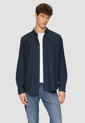 Chemise à manches longues, bleu foncé, avec des boutons, col, poche poitrine, ourlet droit et tissu texturé, portée sur un t-shirt blanc et un jean.