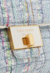 Torebka z tweedu w jasnoniebieskim kolorze z kolorowymi nitkami; posiada złote zapięcie z wygrawerowanym napisem "kate spade NEW YORK" na białej tabliczce.