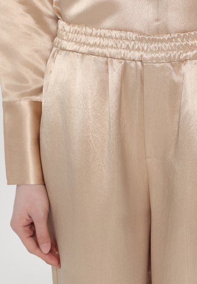 Beige satin loungewear set with an elastic waistband and long sleeves. Fabric has a subtle sheen and a smooth texture.