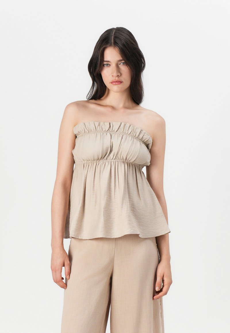 Beige strapless topp med rynket elastisk halslinning og flytende silhuett, laget av lett stoff, parret med matchende beige bukser.