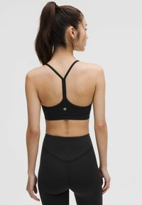 Schwarzer Sport-BH mit Racerback-Design, aus glattem Stoff, mit einem Logo auf der Rückseite. Kombiniert mit schwarzen Leggings in hoher Taille.