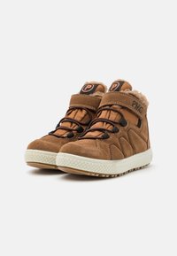 Tan suwede mid-top sko med sorte detaljer, som har en teksturert såle med godt grep, snøring og borrelås, samt en myk, isolert krage.