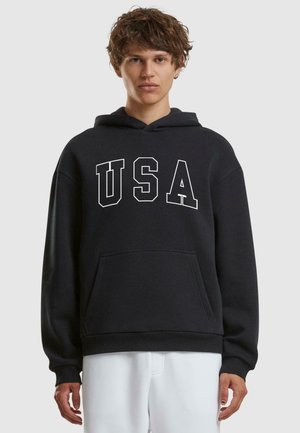 Sort hættetrøje med "USA" i fede hvide bogstaver, med en forlommek for og ribbede manchetter og kant. Blødt stof.