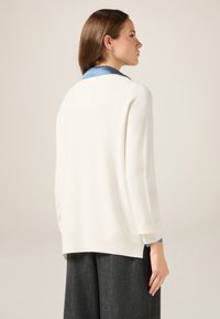 Biały sweter dzianinowy o luźnym kroju, z niebieskim satynowym kołnierzem. Długie rękawy i nieco dłuższy tył o gładkiej strukturze.