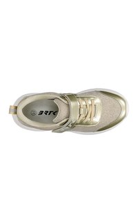 Sneaker ma złotą i beżową tekstylną cholewkę z metalicznymi akcentami, regulowany pasek oraz białą gumową podeszwę. Okrągły czubek.